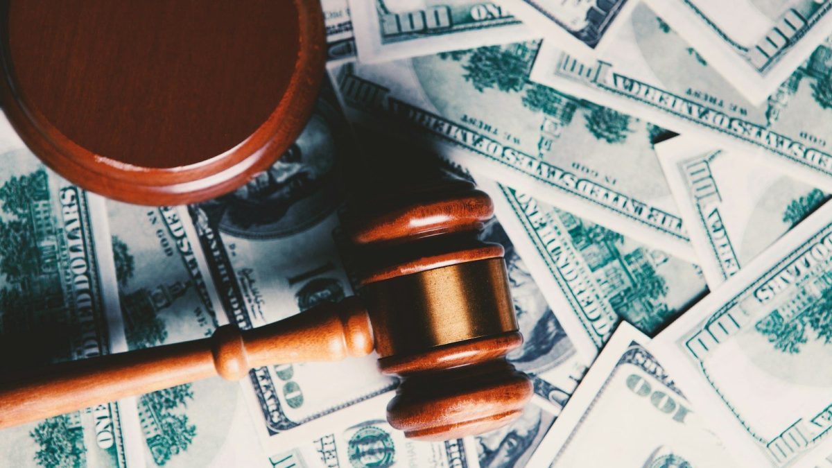 Wooden judge gavel placed over US dollar banknotes representing financial penalties, regulatory fines, enforcement actions, and the cost of non-compliance.