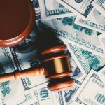 Wooden judge gavel placed over US dollar banknotes representing financial penalties, regulatory fines, enforcement actions, and the cost of non-compliance.