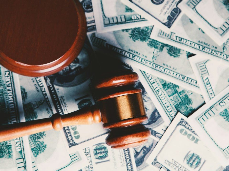 Wooden judge gavel placed over US dollar banknotes representing financial penalties, regulatory fines, enforcement actions, and the cost of non-compliance.